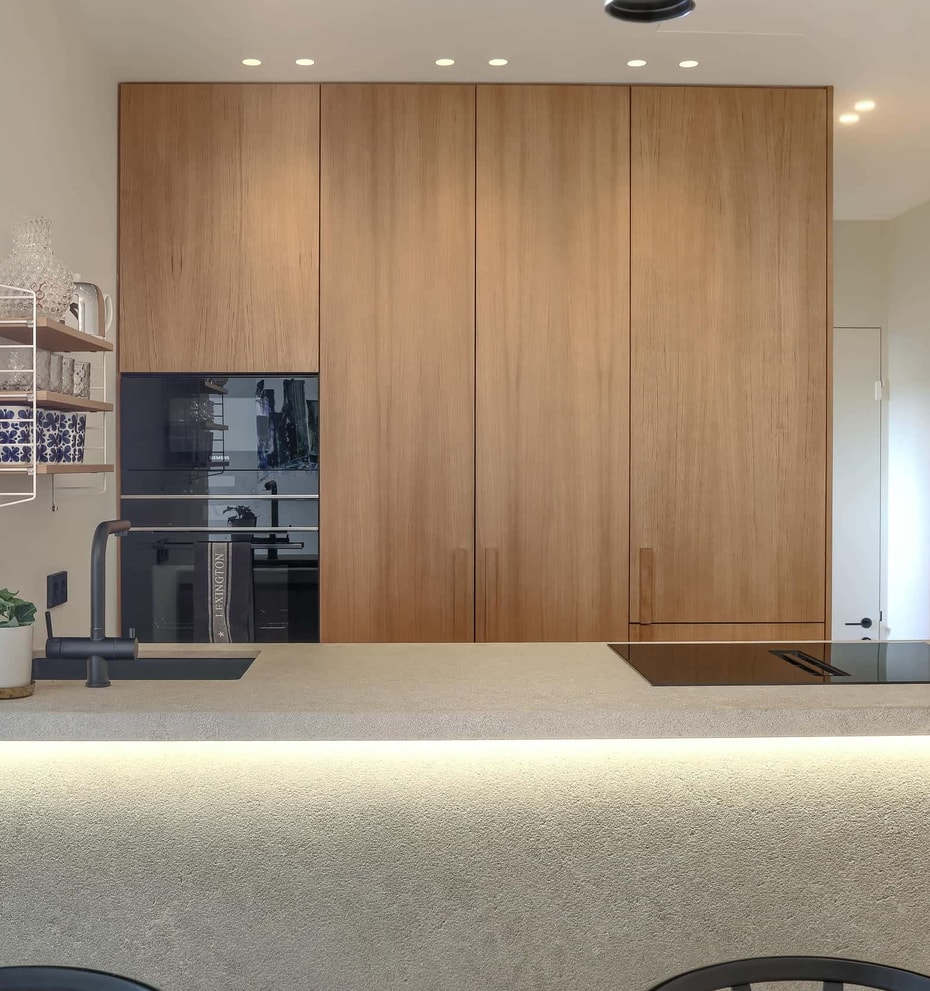 Modern kitchen with full-height oak cabinetry, a light stone kitchen island with integrated LED lighting, and built-in oven.