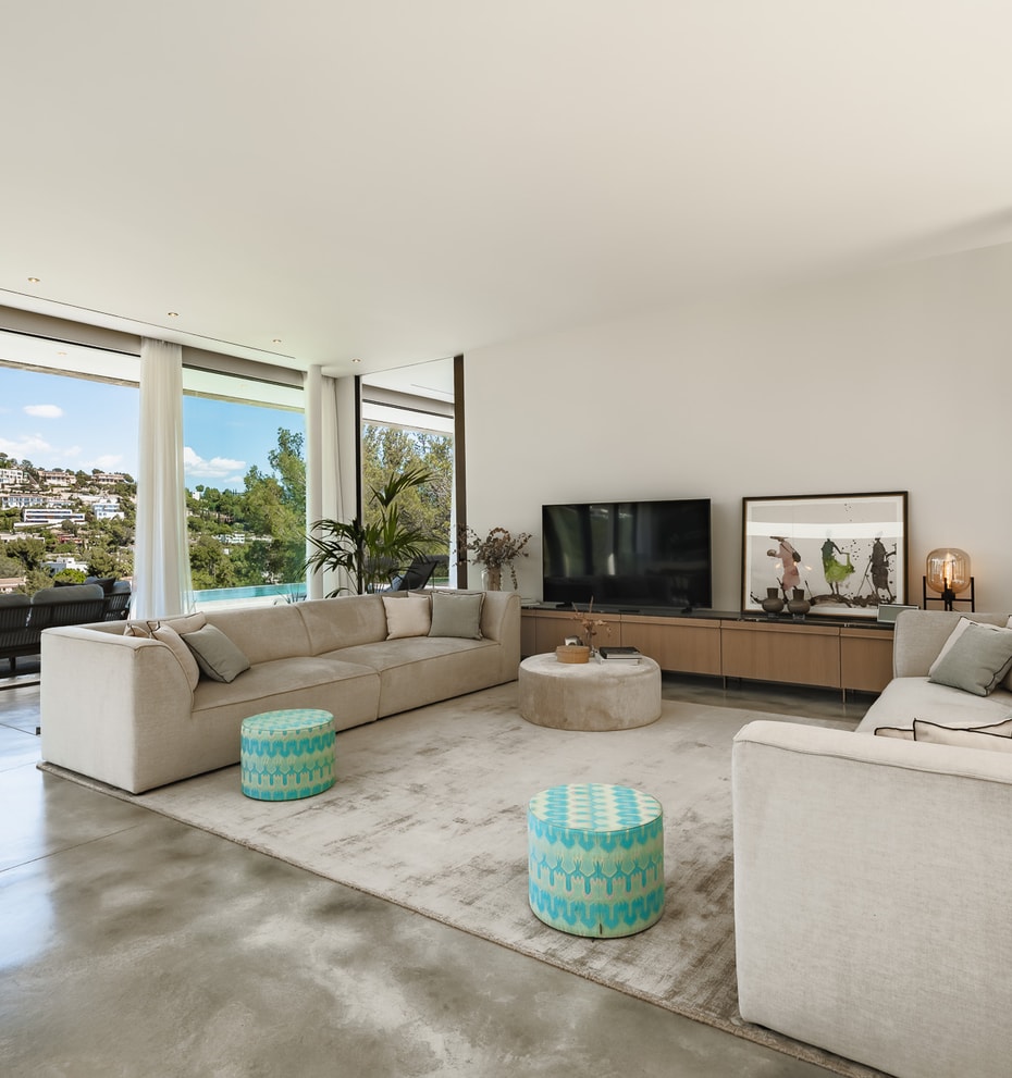 Modern living room with polished concrete floors, modular sofas, and full-height glass doors overlooking the hills.