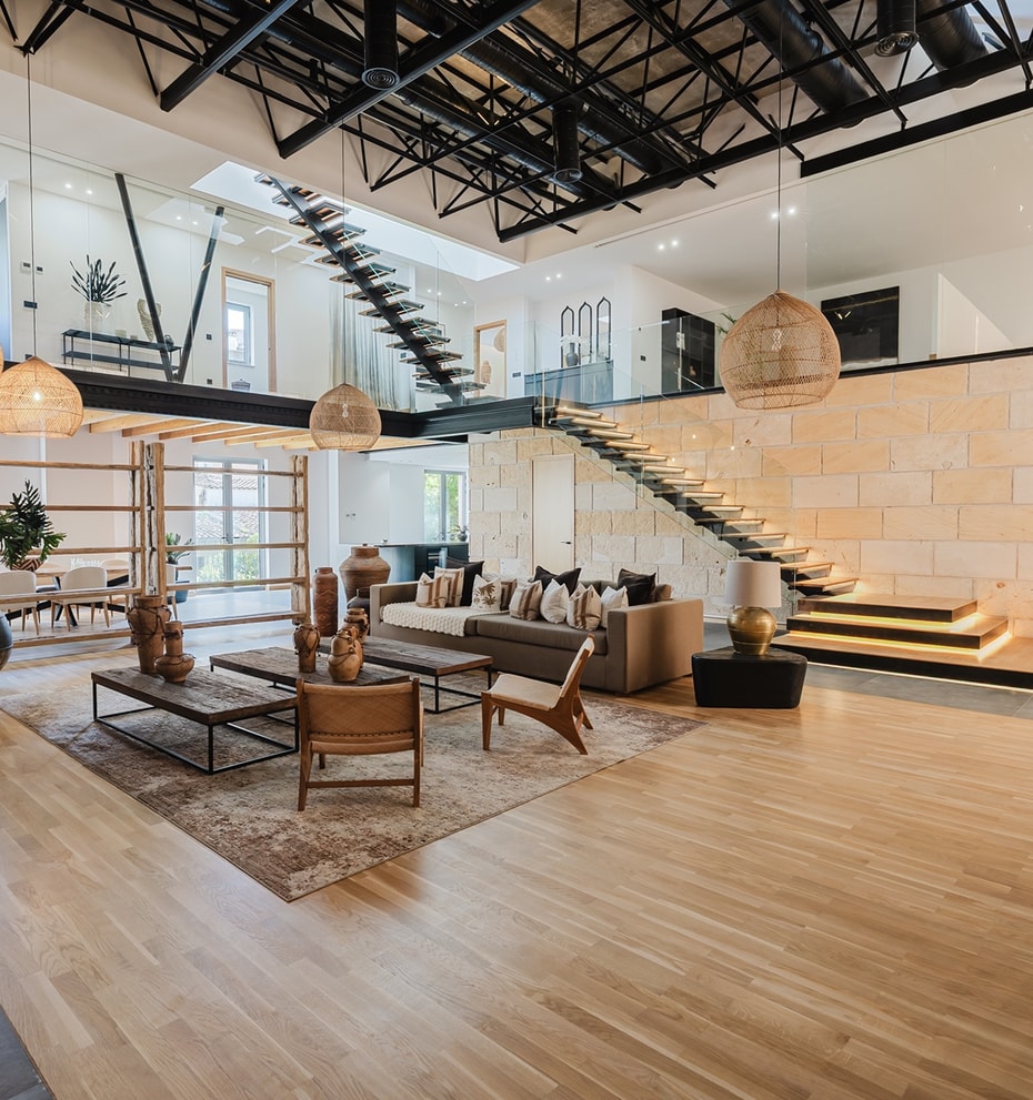Double-height living space with light wood floors, a natural stone feature wall, and a dramatic steel staircase.