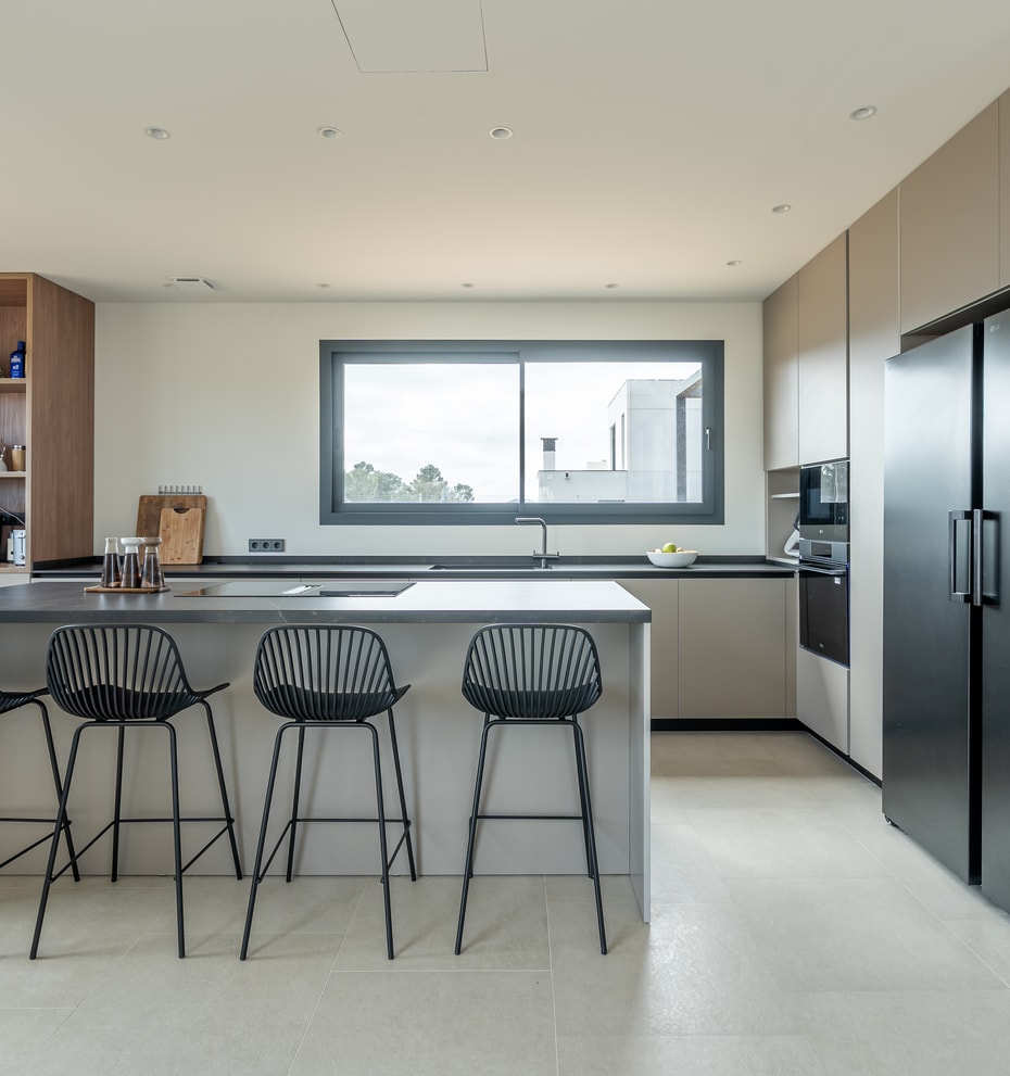 Modern open kitchen with light grey cabinetry, black refrigerator, and a central island with four black wire stools.