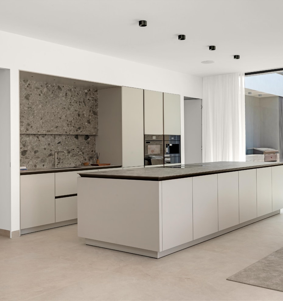 Handleless island kitchen with dark stone worktop, terrazzo-effect splashback and garden views