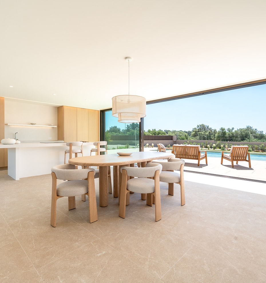 Bright dining area with oval wooden table and cream upholstered chairs, large sliding doors opening to an outdoor pool deck.