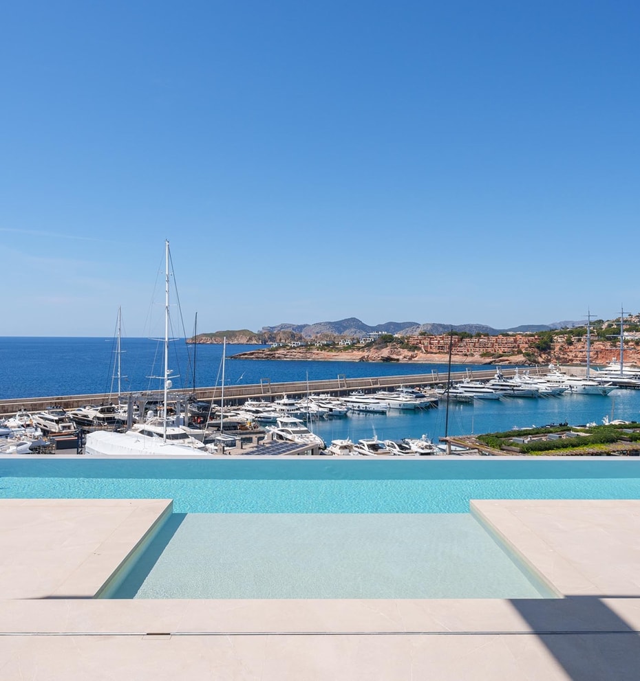 A rectangular infinity pool with turquoise water in the foreground, framing a direct view of the marina and yachts.
