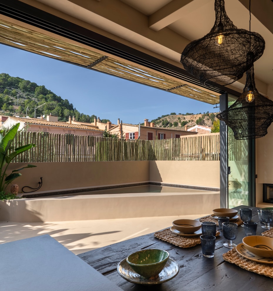 Dining room with large sliding doors opening to an outdoor terrace with a pool, overlooking a hillside.