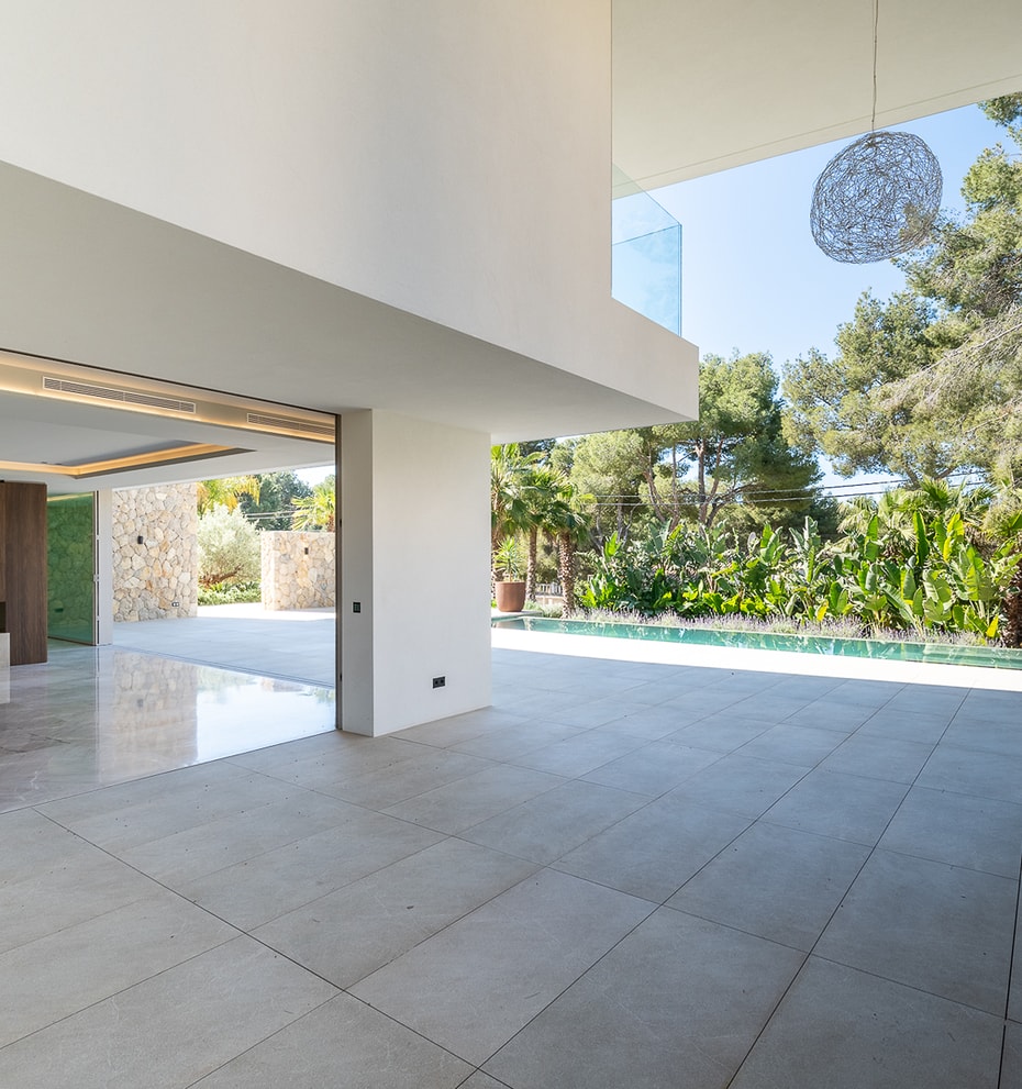 Interior view of a contemporary living area with large floor-to-ceiling glass doors opening onto a sunlit pool terrace.