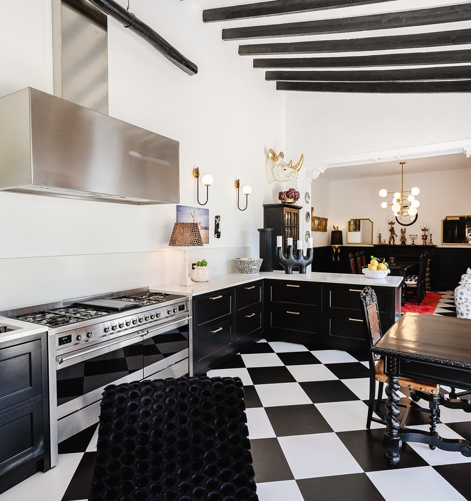 Kitchen features black and white checkered tile floors, black cabinets, a stainless steel range, and exposed dark wood beams.