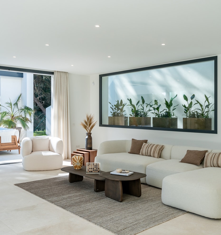 Spacious open-plan living room with bouclé sofas, stone flooring and floor-to-ceiling sliding doors opening to the pool terrace