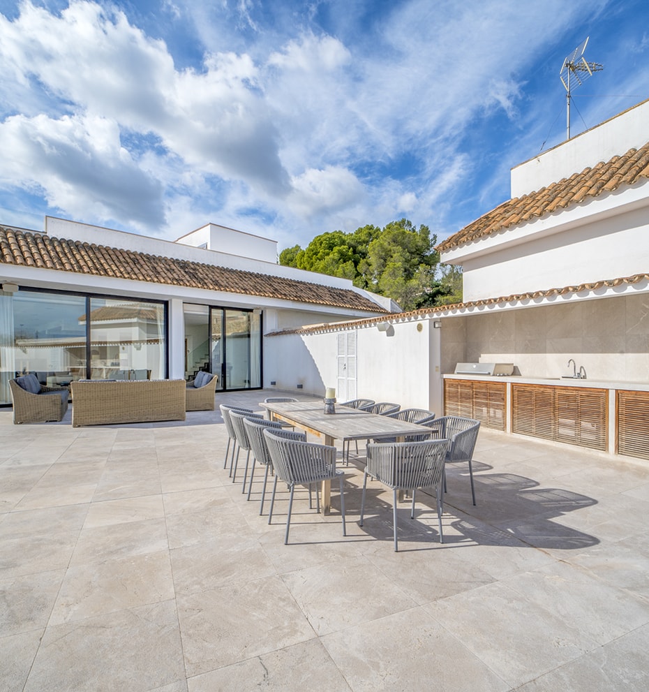 A spacious terrace in Illetas featuring a dining set, an outdoor kitchen with wooden cabinetry, and large sliding glass doors.