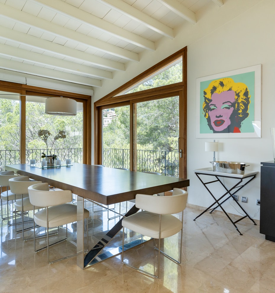 Large open-plan reception room with white beam ceilings, marble floors and art-hung wall leading to dining area