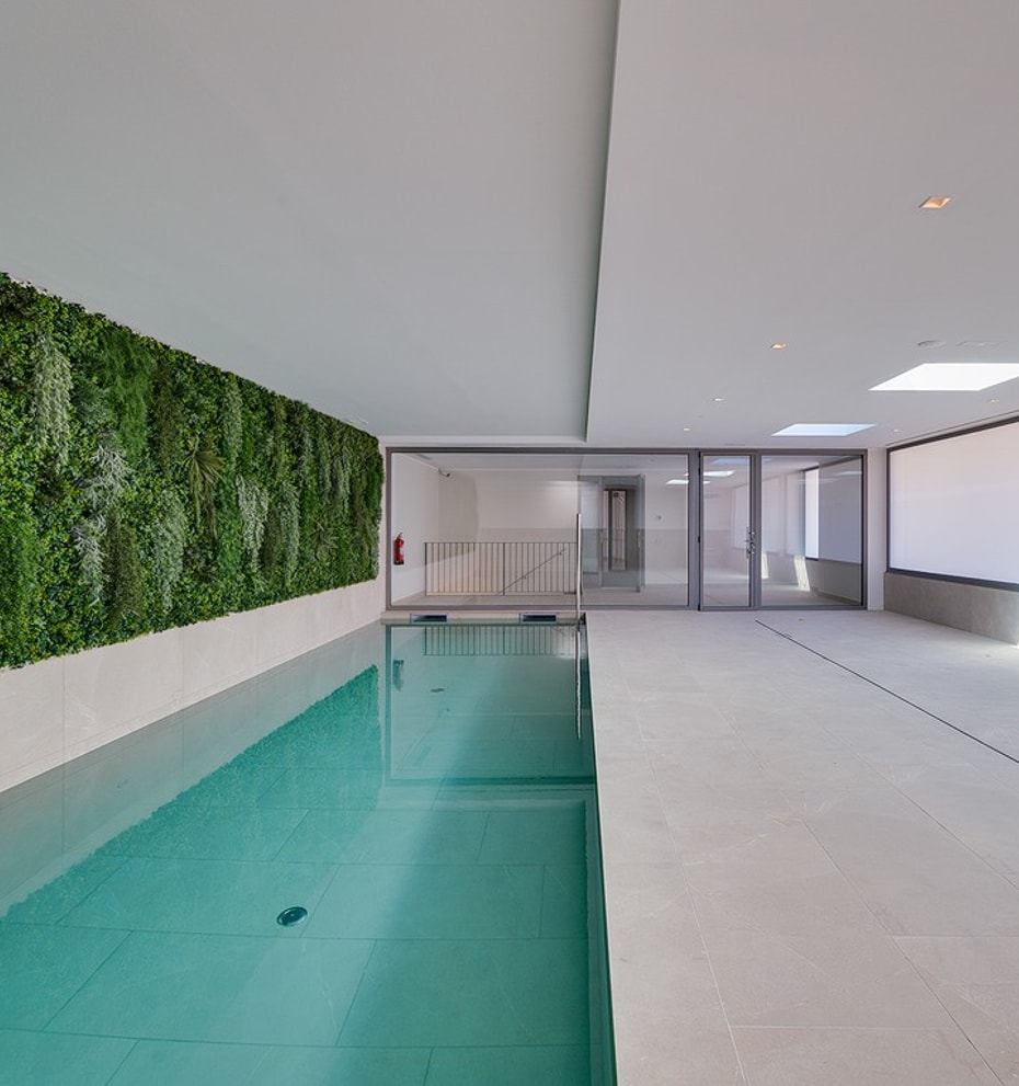 Rectangular indoor lap pool with full-length living plant wall to one side, skylights above and floor-to-ceiling glazing at the far end