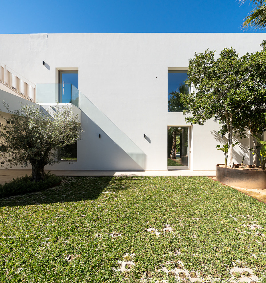 Modern white minimalist villa exterior featuring a flat roof, large rectangular windows, and a manicured green lawn with mature trees.