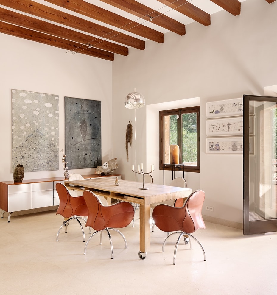 Dining room in a Finca featuring a long wooden table, leather swivel chairs, exposed ceiling beams, and a terrace doorway.