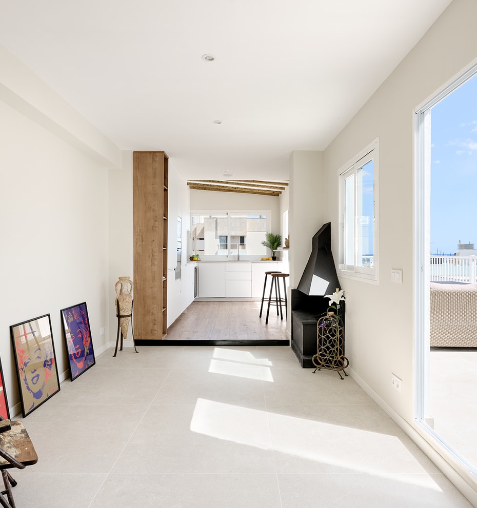 Bright living area with white walls, tile floors, and a corner fireplace, leading to an outdoor terrace with sea views.