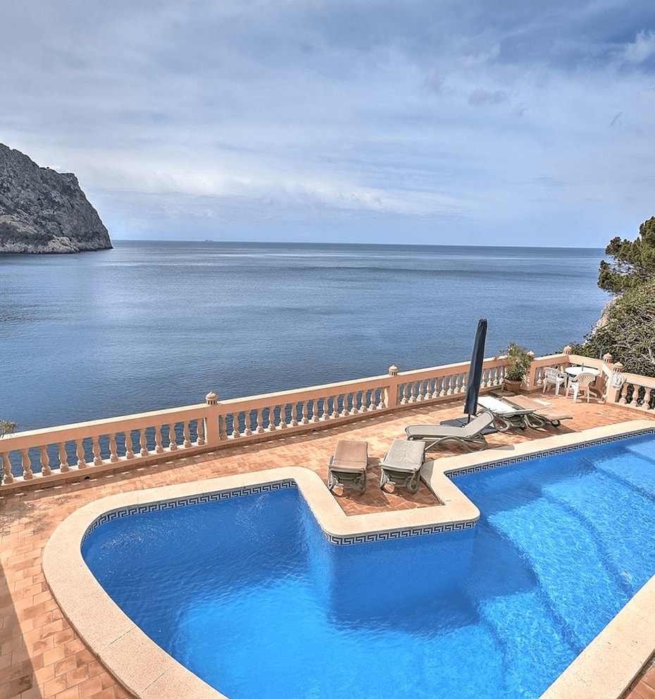 An L-shaped swimming pool with blue water sits on a terracotta-tiled terrace overlooking the sea at Cala Llamp.