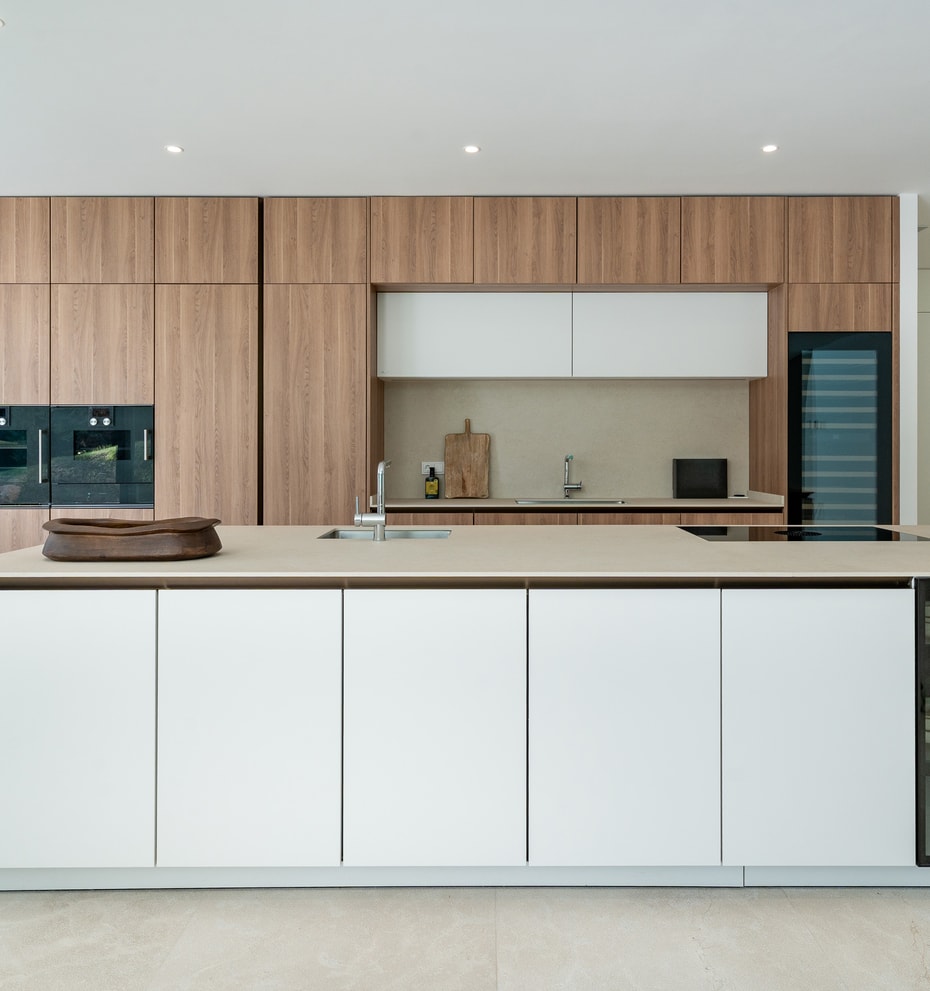 White handleless Siematic kitchen island with stone worktop, integrated sink and glass-fronted crockery display, floor-to-ceiling oak-veneer cabinetry and Gaggenau ovens behind