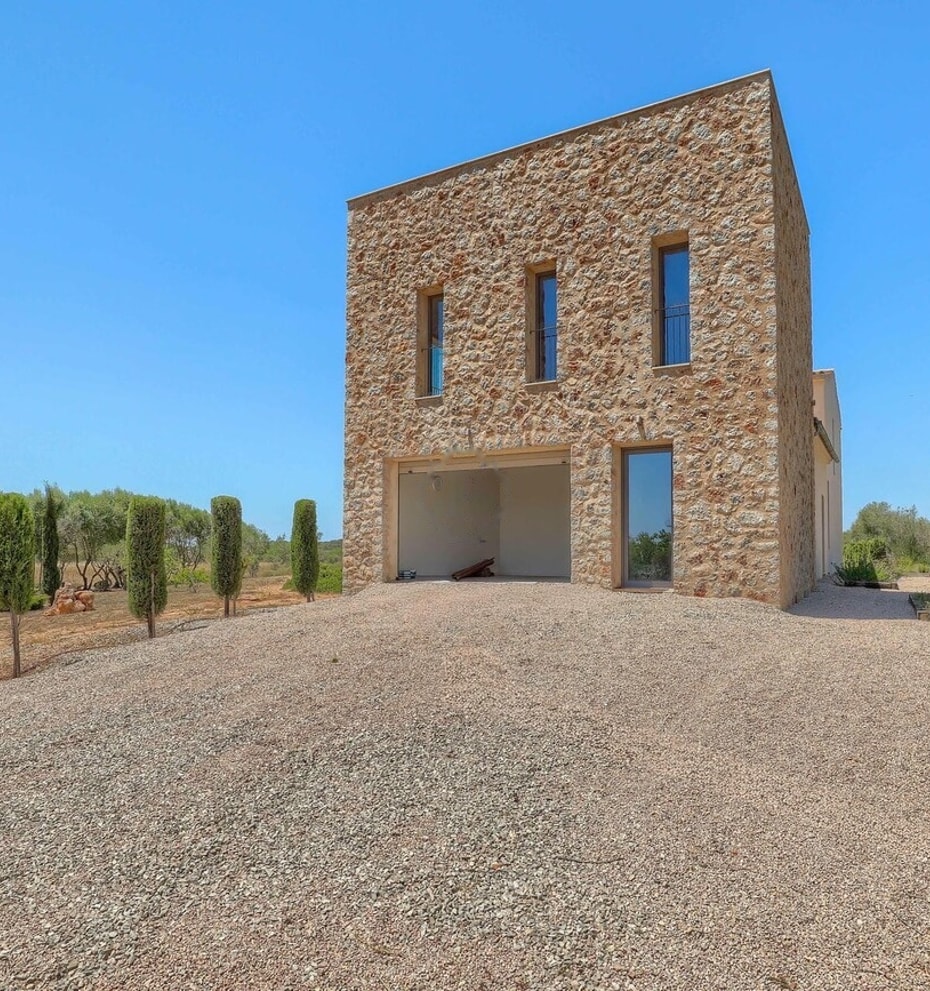Two-story stone-clad outbuilding with narrow windows and an open ground-level portico, set against a gravel driveway.