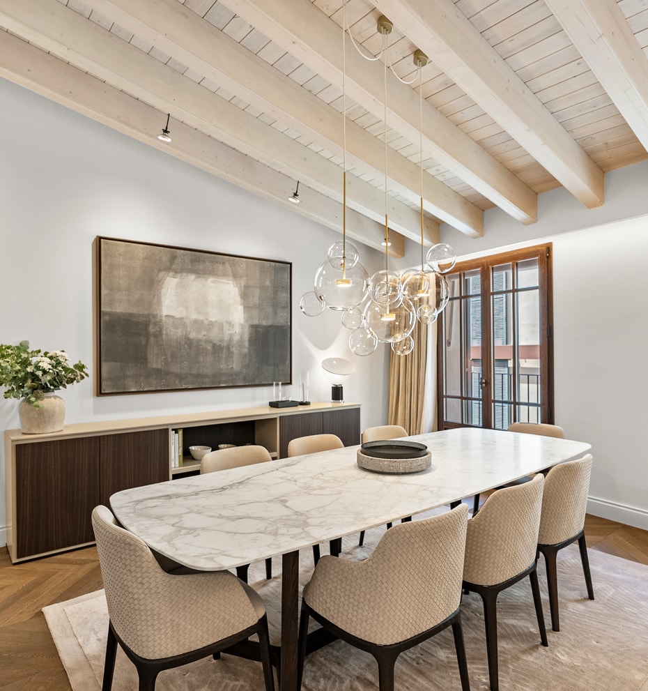 Contemporary dining room featuring a white marble table, upholstered chairs, and exposed white-washed ceiling beams.