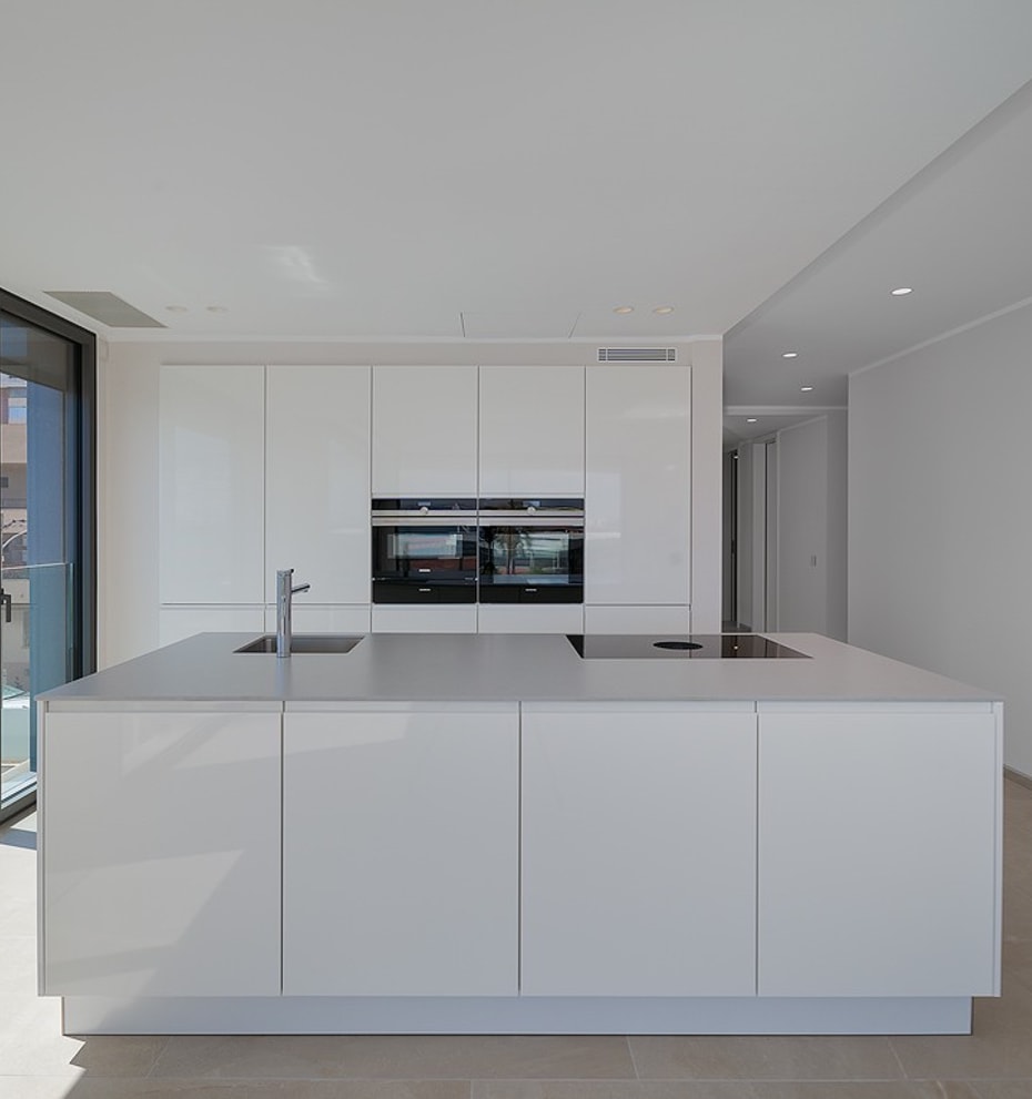 Integrated white kitchen and living area with large sliding glass doors opening to terrace and sea view