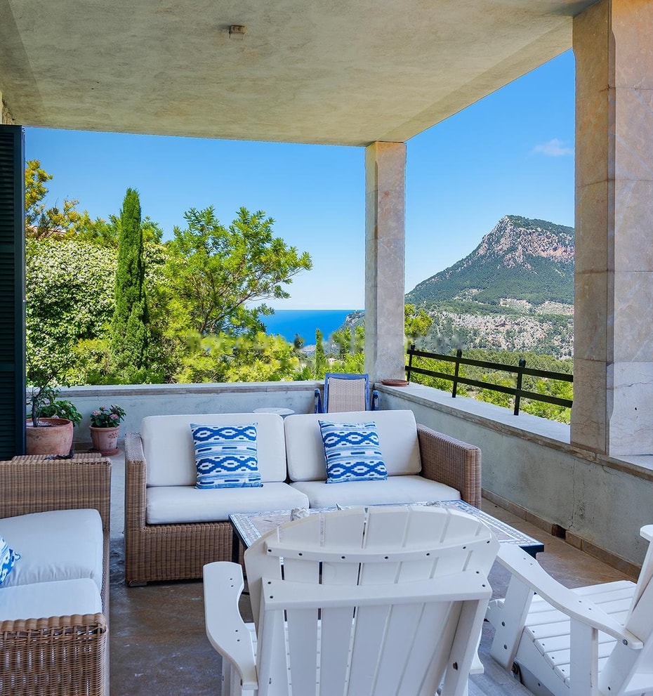 Large covered terrace with fireplace, multiple seating zones, and uninterrupted view across forested valley to distant mountains