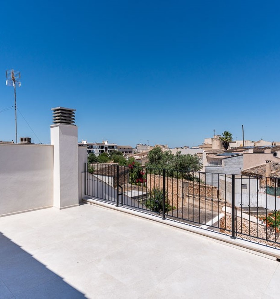 An open, paved rooftop terrace with white walls and a black metal railing overlooking the traditional tiled roofs of Campos.