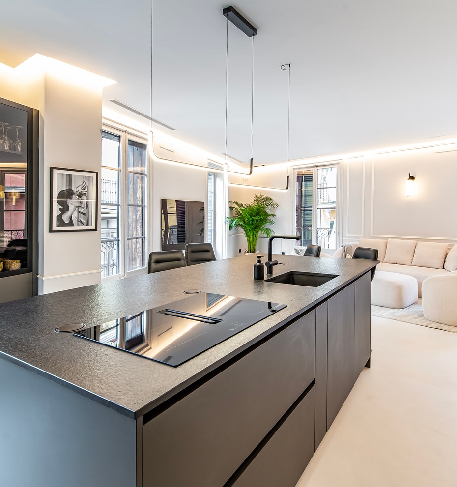 Modern open-plan kitchen with a large dark charcoal island, integrated appliances, and recessed lighting, overlooking a bright living area.