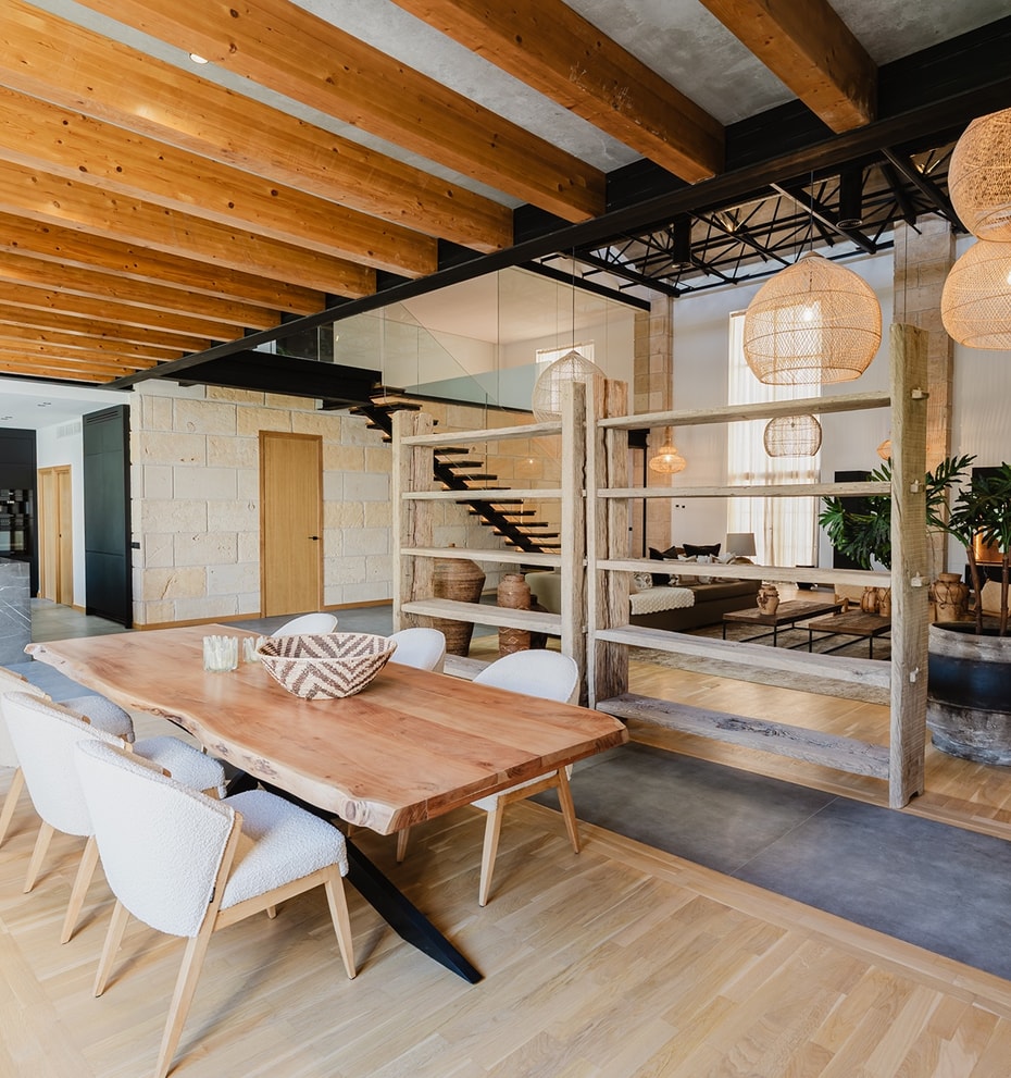 Dining room with a live-edge wooden table, wicker pendant lights, and exposed wooden ceiling beams in a loft-style apartment.