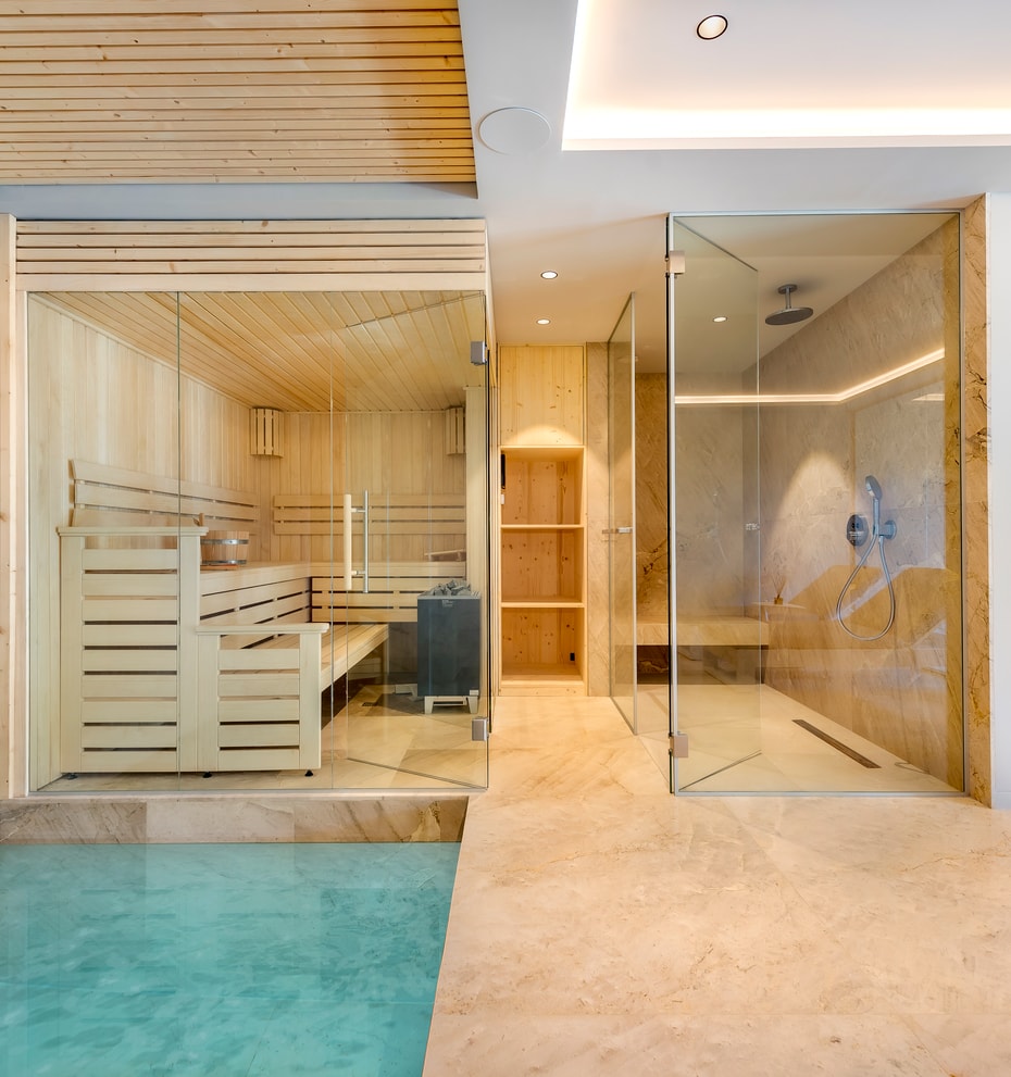 Modern home spa featuring a glass-enclosed cedar sauna beside a walk-in rainfall shower with stone flooring.