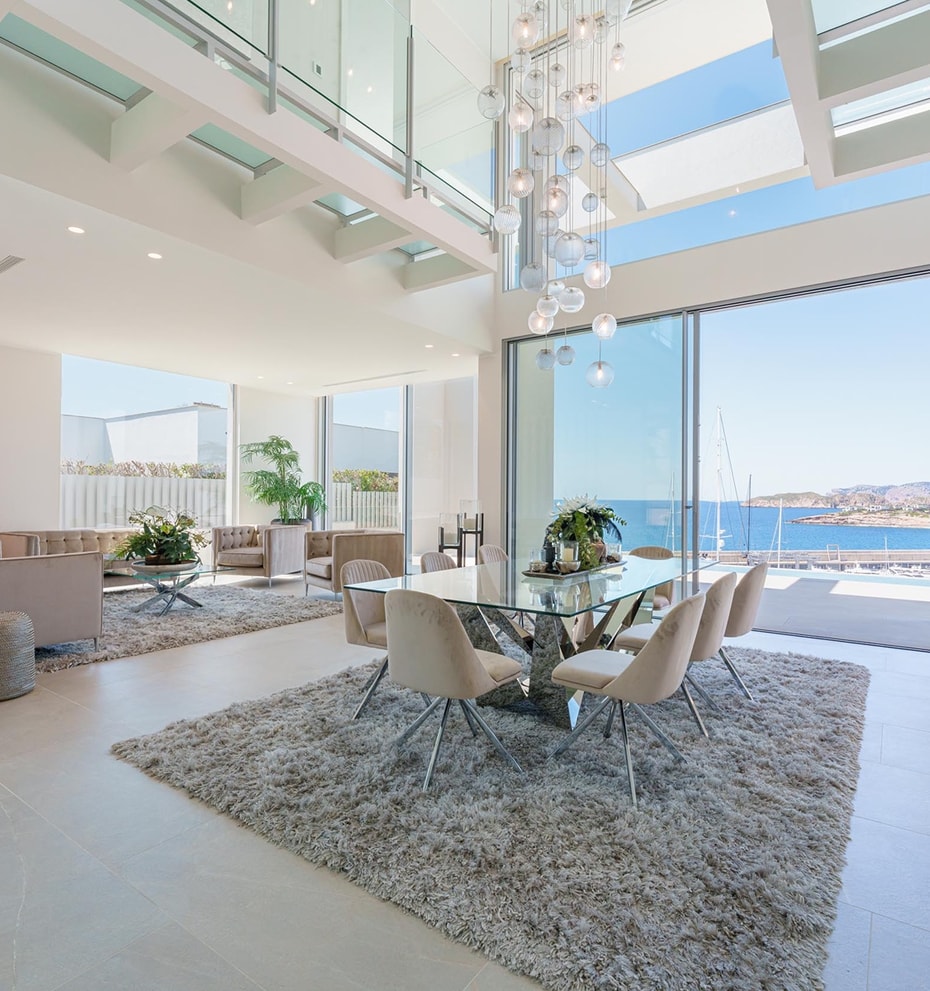 Double-height living and dining space with floor-to-ceiling sliding glass doors opening to a coastal view.